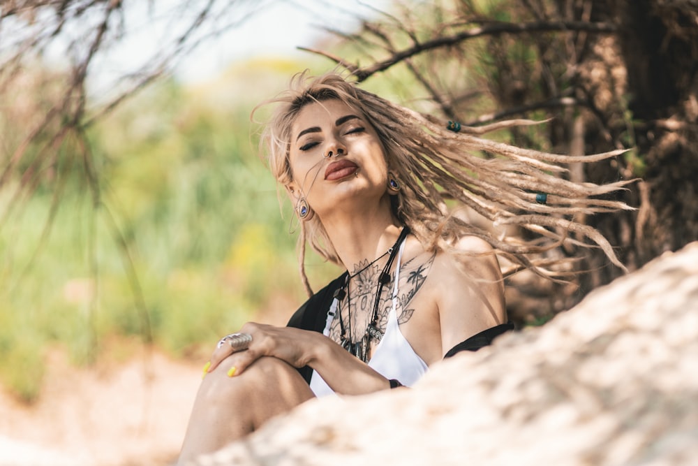 a woman sitting on a rock with her hair blowing in the wind