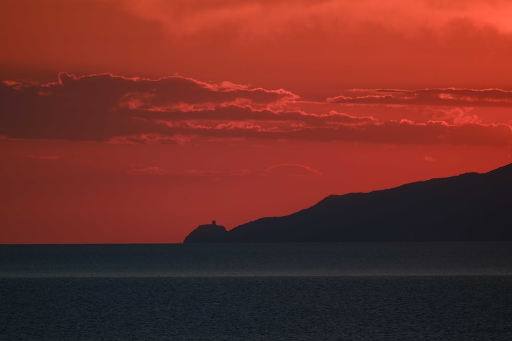 the sun is setting over the ocean with a small island in the distance