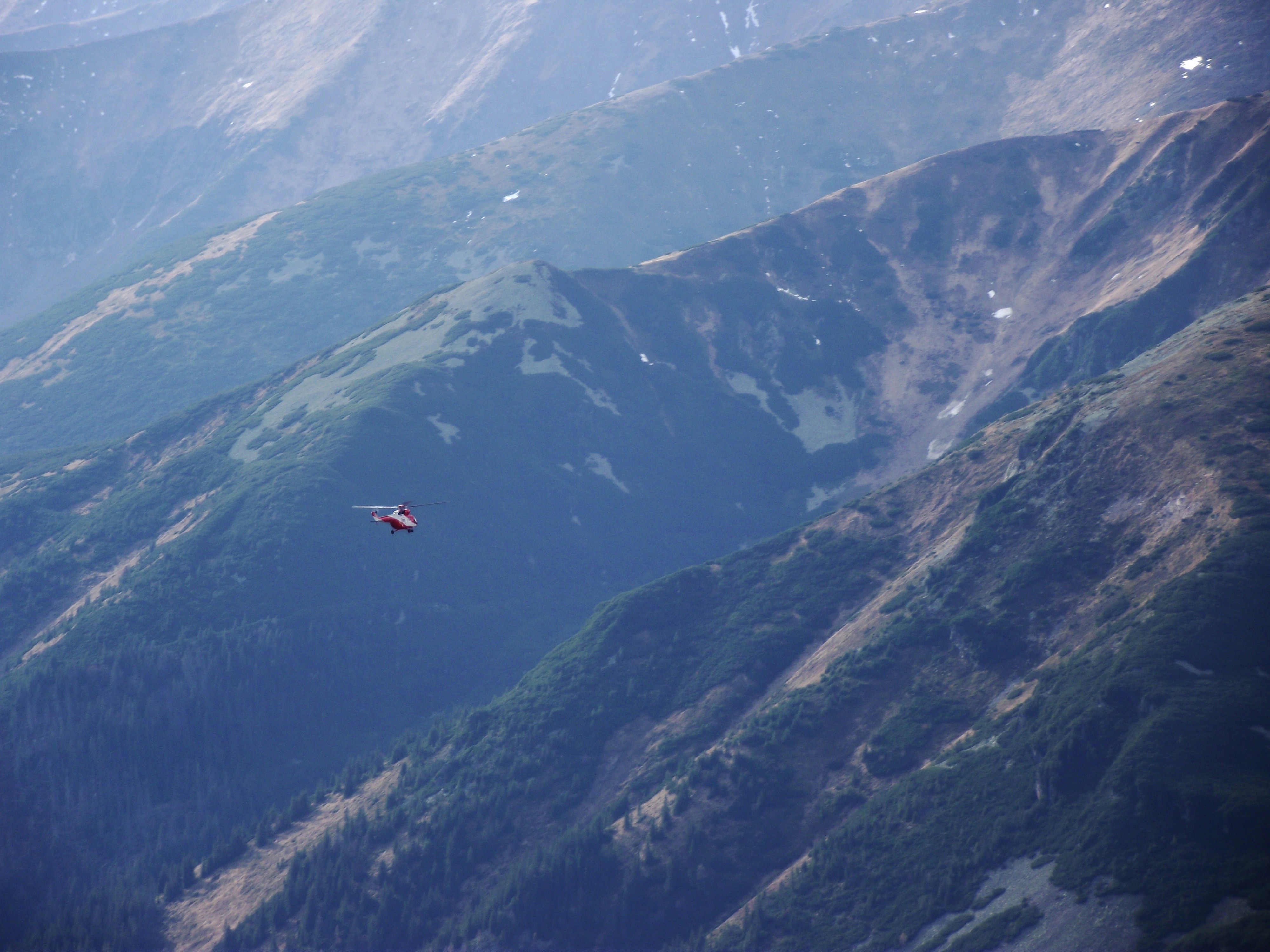 a red helicopter flying over a mountain range