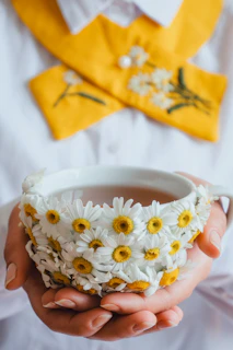 a person holding a cup with daisies in it