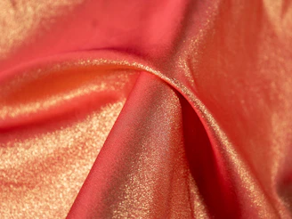 A close-up of soft, shimmering rose gold fabric draped elegantly over a sleek black hanger.