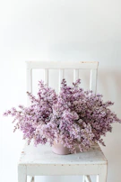 Delicate orchid bouquet draped over a vintage wooden stool in a minimalist room.