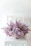 A delicate silk flower arrangement in pastel pink and lavender tones on a minimalist wooden table.