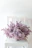 A delicate silk flower arrangement in pastel pink and lavender tones on a minimalist wooden table.