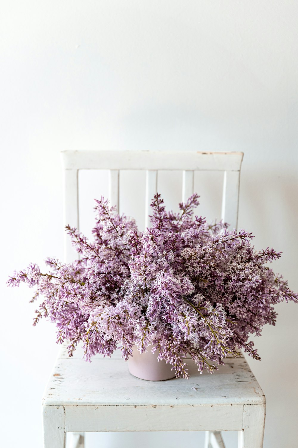 una sedia bianca con un vaso rosa pieno di fiori viola