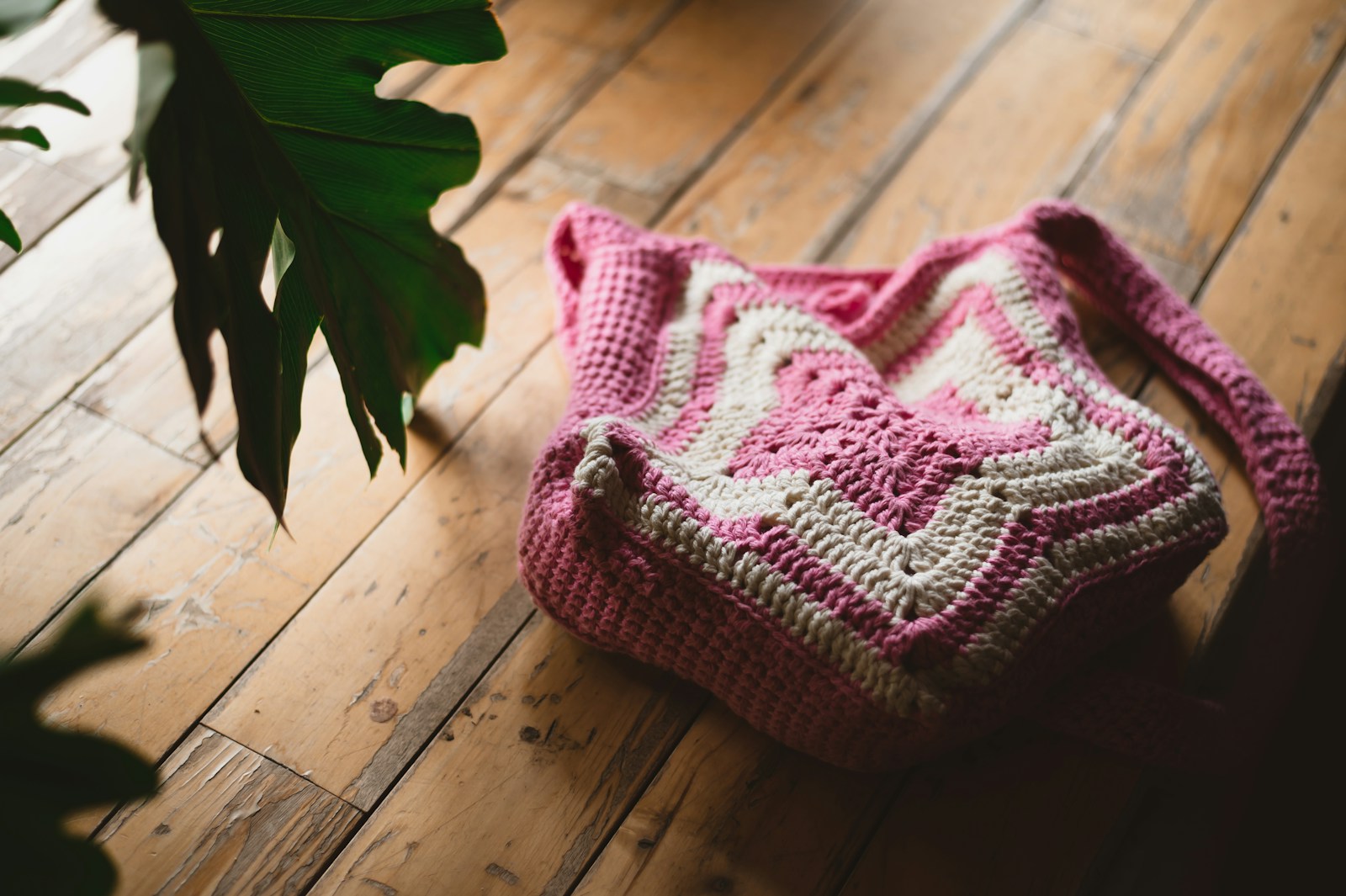 Bolsa de crochê rosa e branca sobre piso de madeira
