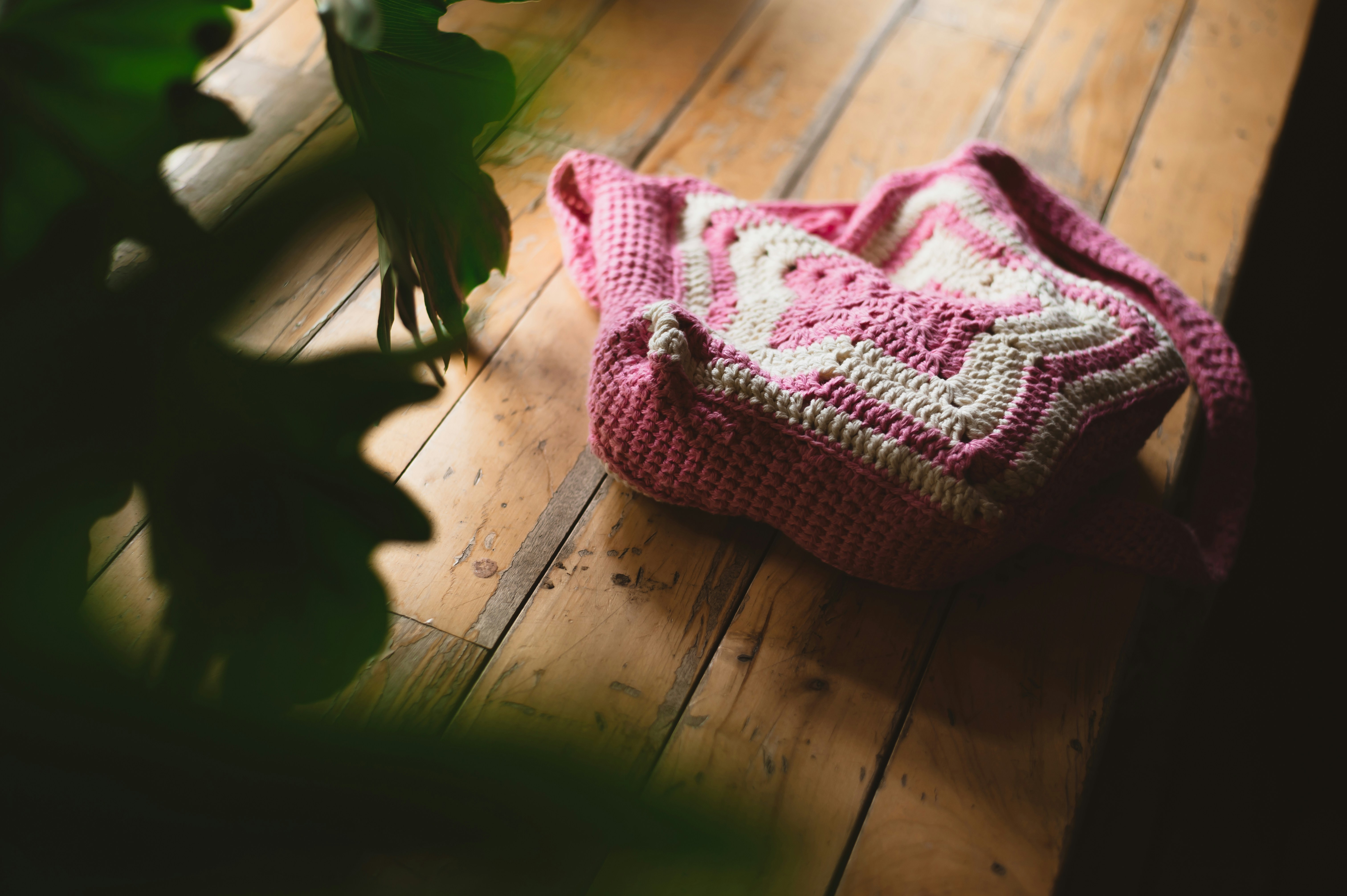 a crocheted bag sitting on a wooden floor next to a potted plant