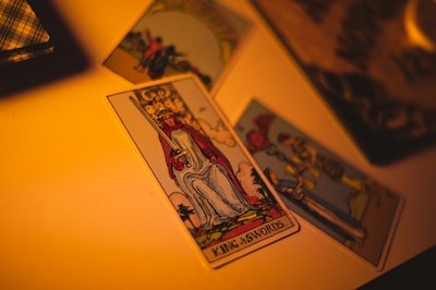 Several tarot cards are laid out on a surface, with a focus on the 'King of Swords' card. The lighting is warm and creates a mysterious atmosphere.