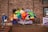 A colorful balloon arrangement with various shapes and sizes is displayed against a brick wall. A person in a blue jacket and jeans is walking down a nearby staircase holding onto the railing. There are windows with signage and a banner displaying text behind the balloons.