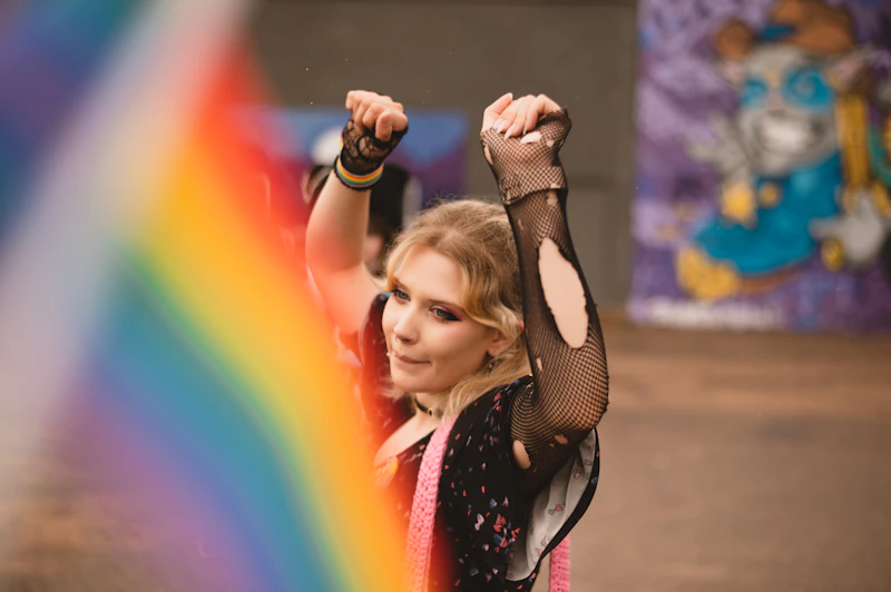 Femboy with arms up, with a rainbow in the background