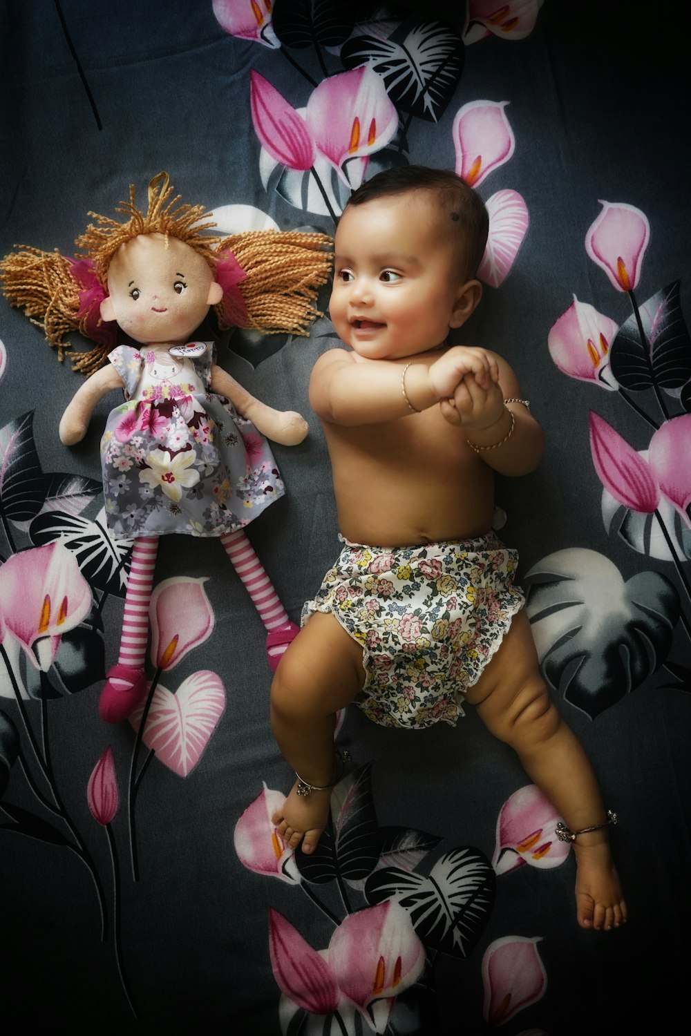 a baby and a doll laying on a bed of flowers