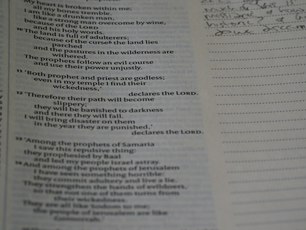 An open book with text on the left page, which appears to be a religious scripture, possibly from the Bible. The right page is lined, intended for taking notes, with some handwritten notes visible in cursive.