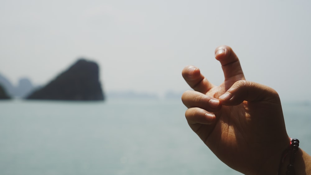 a person is holding their hand up in front of a body of water