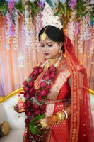 A bride wearing a rich red Rajput wedding dress adorned with gold jewelry, standing in a royal courtyard.