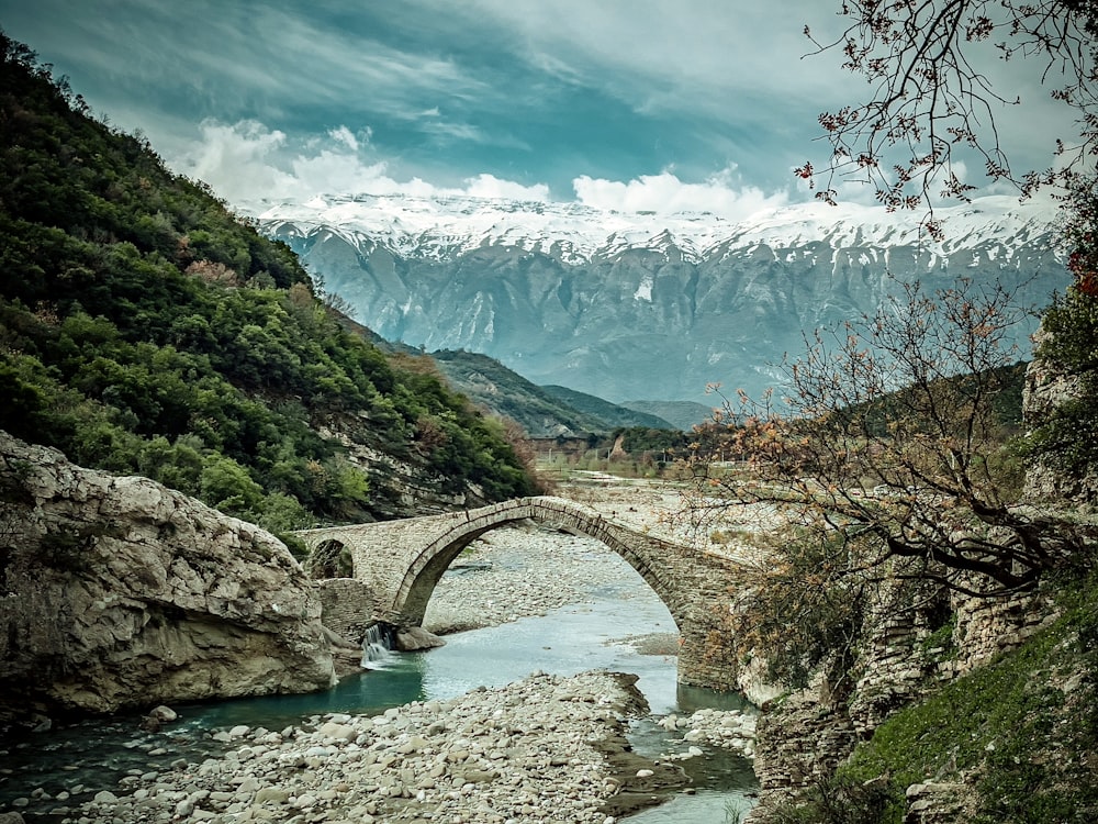 a stone bridge over a river with mountains in the background