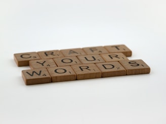 Wooden tiles resembling game pieces are arranged to spell out the phrase 'CRAFT YOUR WORDS' on a plain surface.