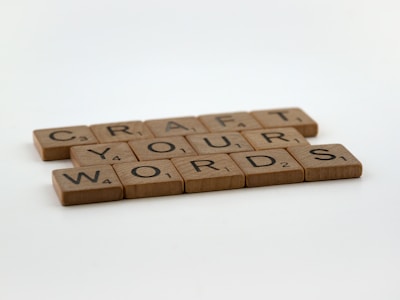 Wooden tiles resembling game pieces are arranged to spell out the phrase 'CRAFT YOUR WORDS' on a plain surface.