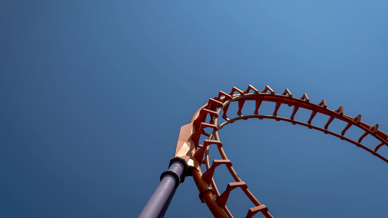 A roller coaster track rising and falling against a blue sky