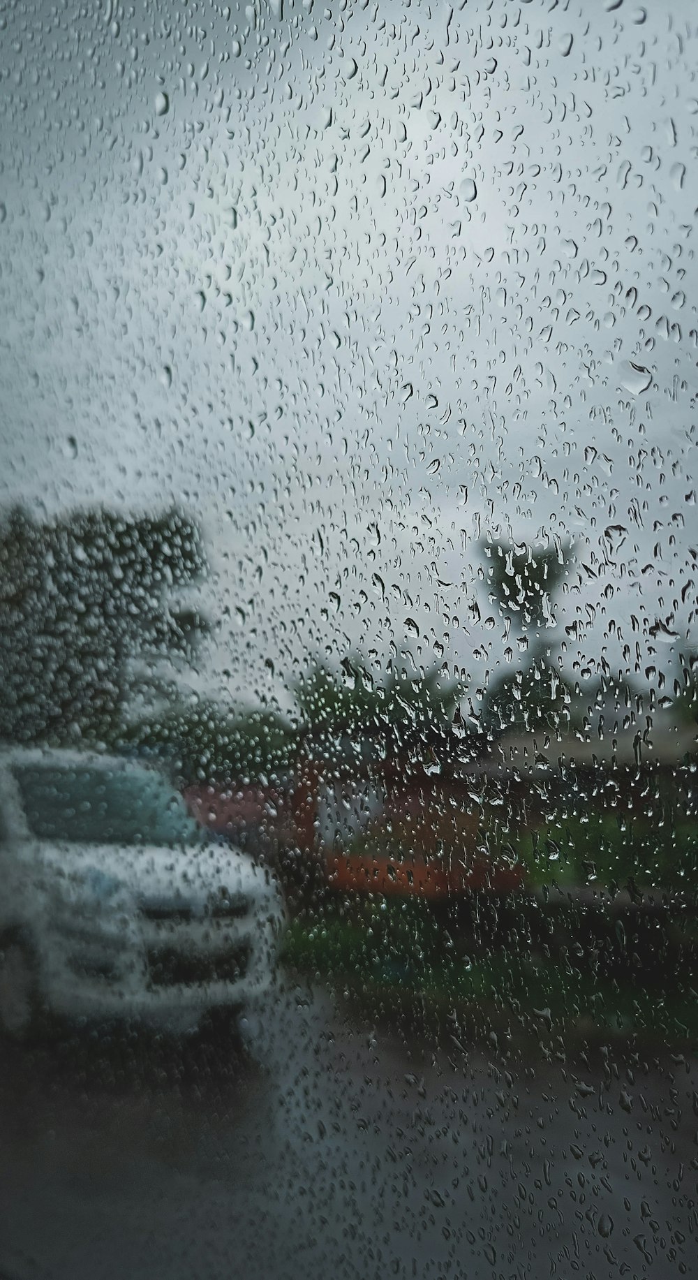 a rain covered window with cars parked in the background