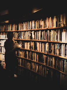 A scholar reviewing a manuscript in a sunlit library filled with classic books