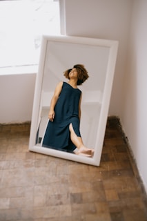 A sleek full-length standing mirror positioned near a bright window with sheer curtains.