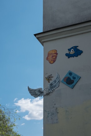 A wall is adorned with various artistic designs and graphics, including a depiction of a stylized face, a cartoon character in blue, and a relief sculpture of an angelic face with wings. There's also an abstract pattern on a blue square plaque.