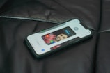 A smartphone lies on a dark leather surface, displaying a contact screen with an image of a person and controls for calling or messaging.