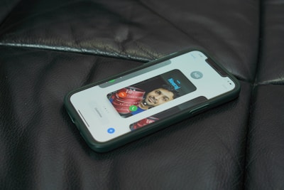 A smartphone lies on a dark leather surface, displaying a contact screen with an image of a person and controls for calling or messaging.