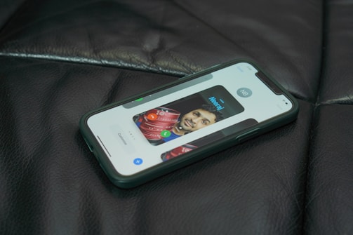 A smartphone lies on a dark leather surface, displaying a contact screen with an image of a person and controls for calling or messaging.