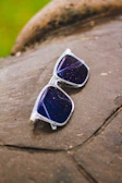 Sunlit outdoor shot featuring sunglasses with a subtle star motif reflecting the bright sky.