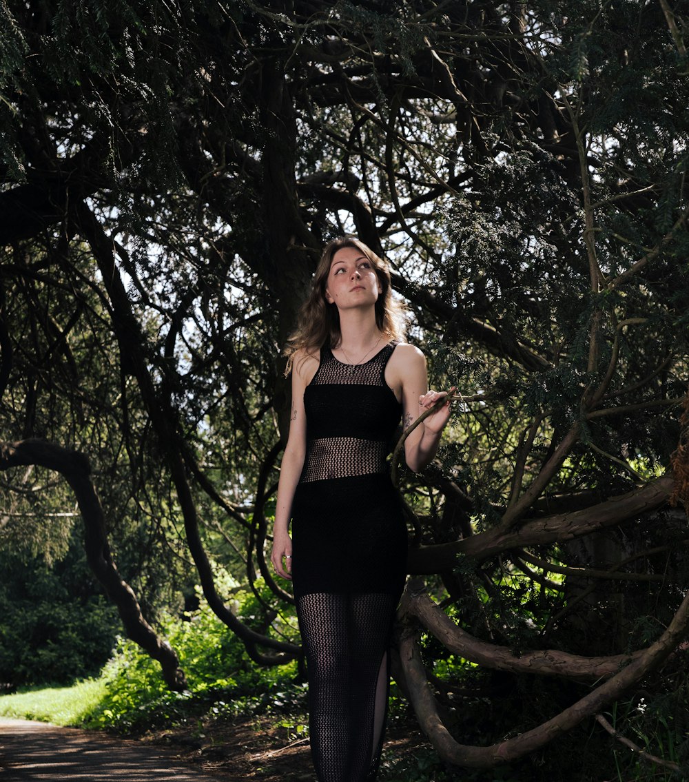 a woman in a black dress standing in front of a tree