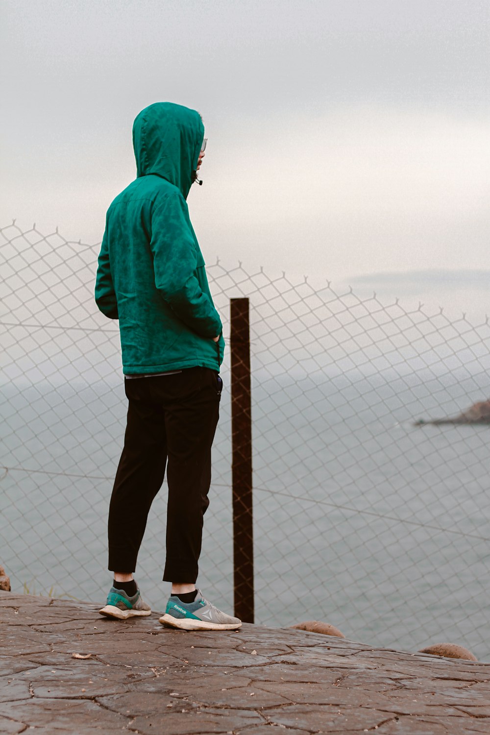 a person in a green hoodie looking at the ocean
