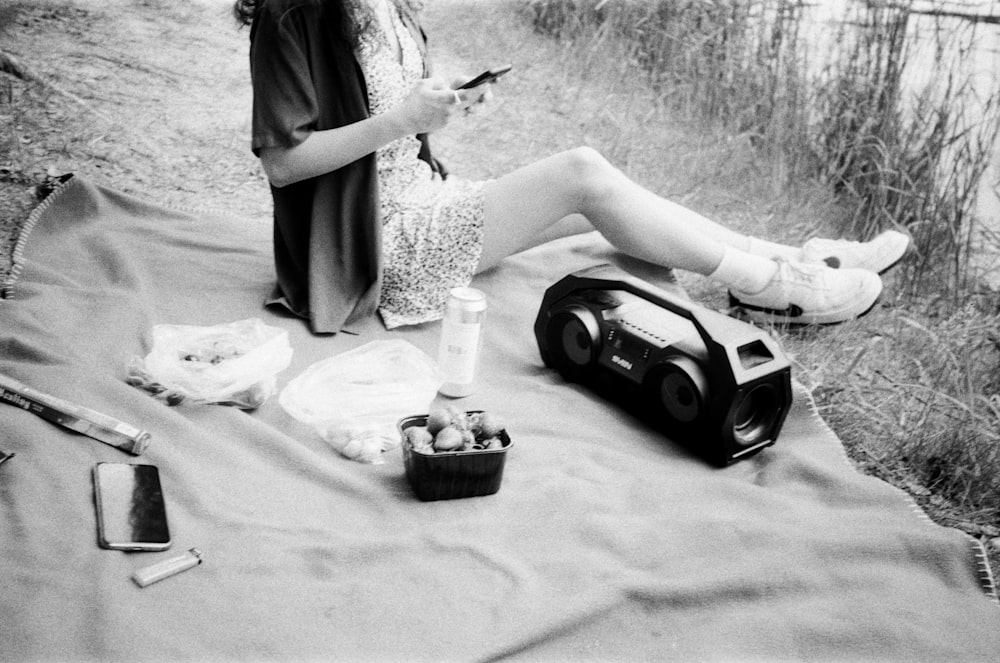 a woman sitting on top of a blanket holding a cell phone