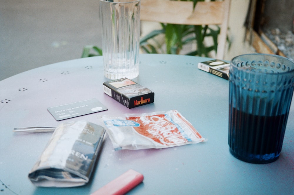 a glass of water, a cell phone, and some cigarettes on a table