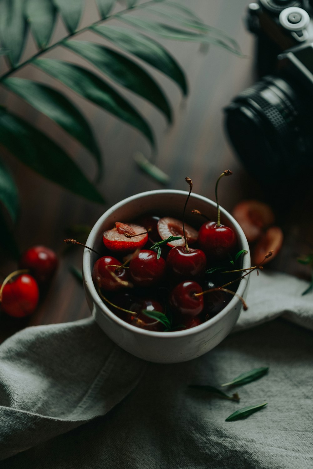 a white bowl filled with cherries next to a camera