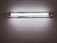 A fluorescent light fixture is mounted on a white tiled wall. The light is turned on, casting a bright, even glow across the surrounding tiles. The fixture contains two fluorescent tubes, enclosed in a metallic frame.