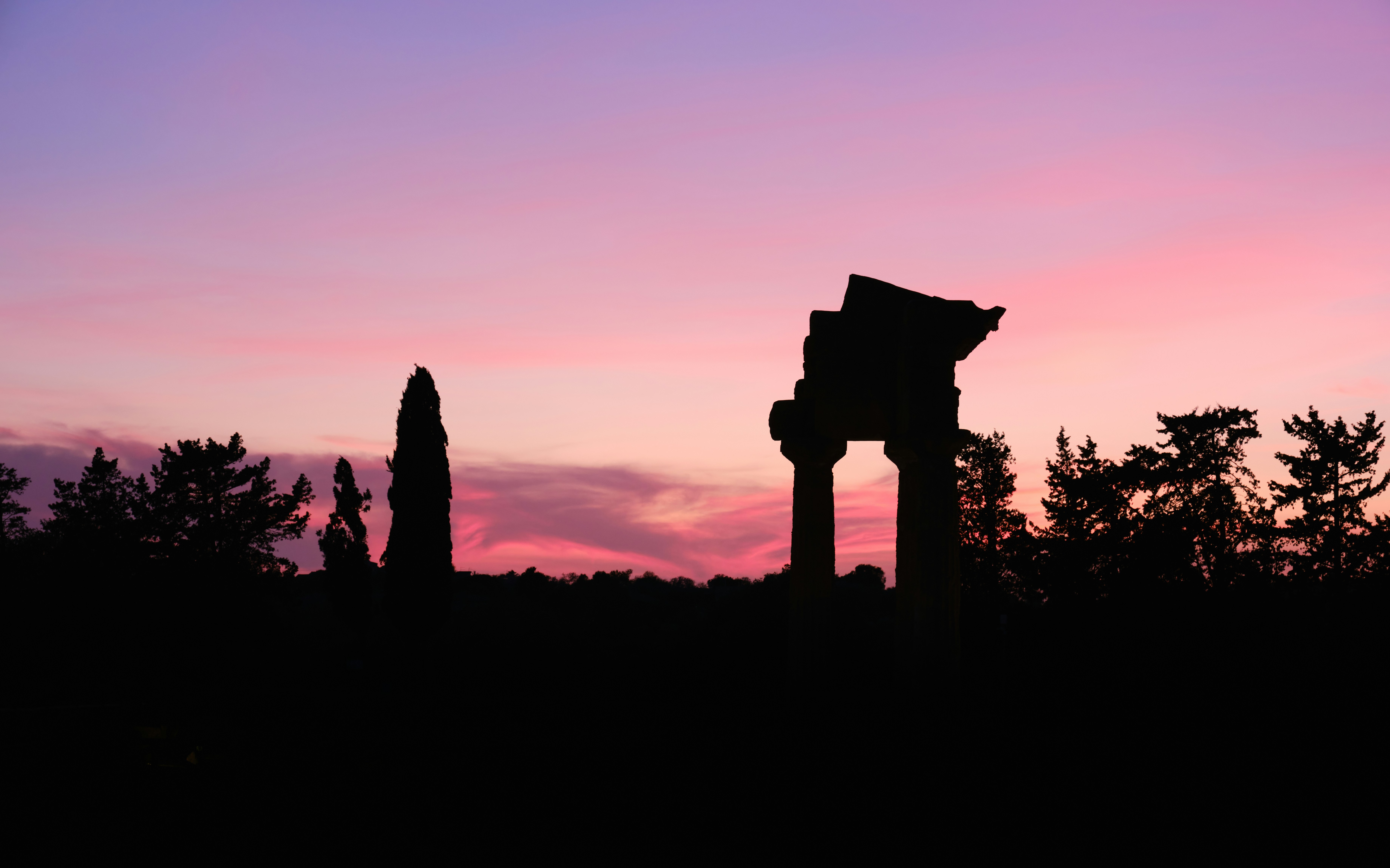 the silhouette of a building against a pink and purple sky, Valley of the temples in Agrigento, Sicily