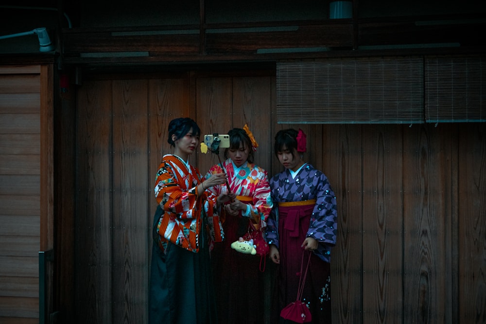 three geisha girls standing in front of a wooden wall