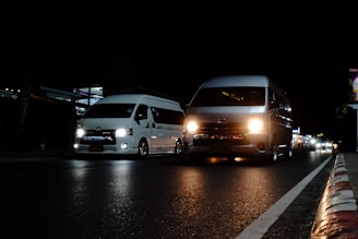 a couple of white vans driving down a street at night