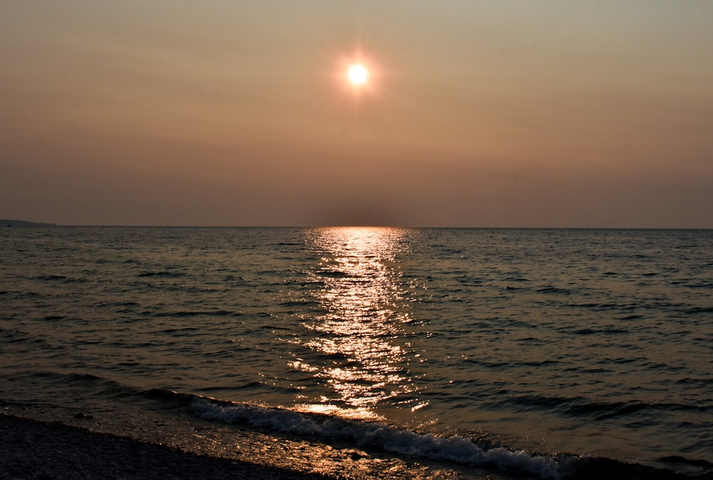 the sun is setting over the water at the beach