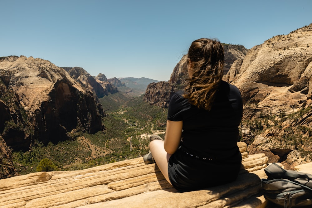 a woman sitting on a rock looking out over a valley