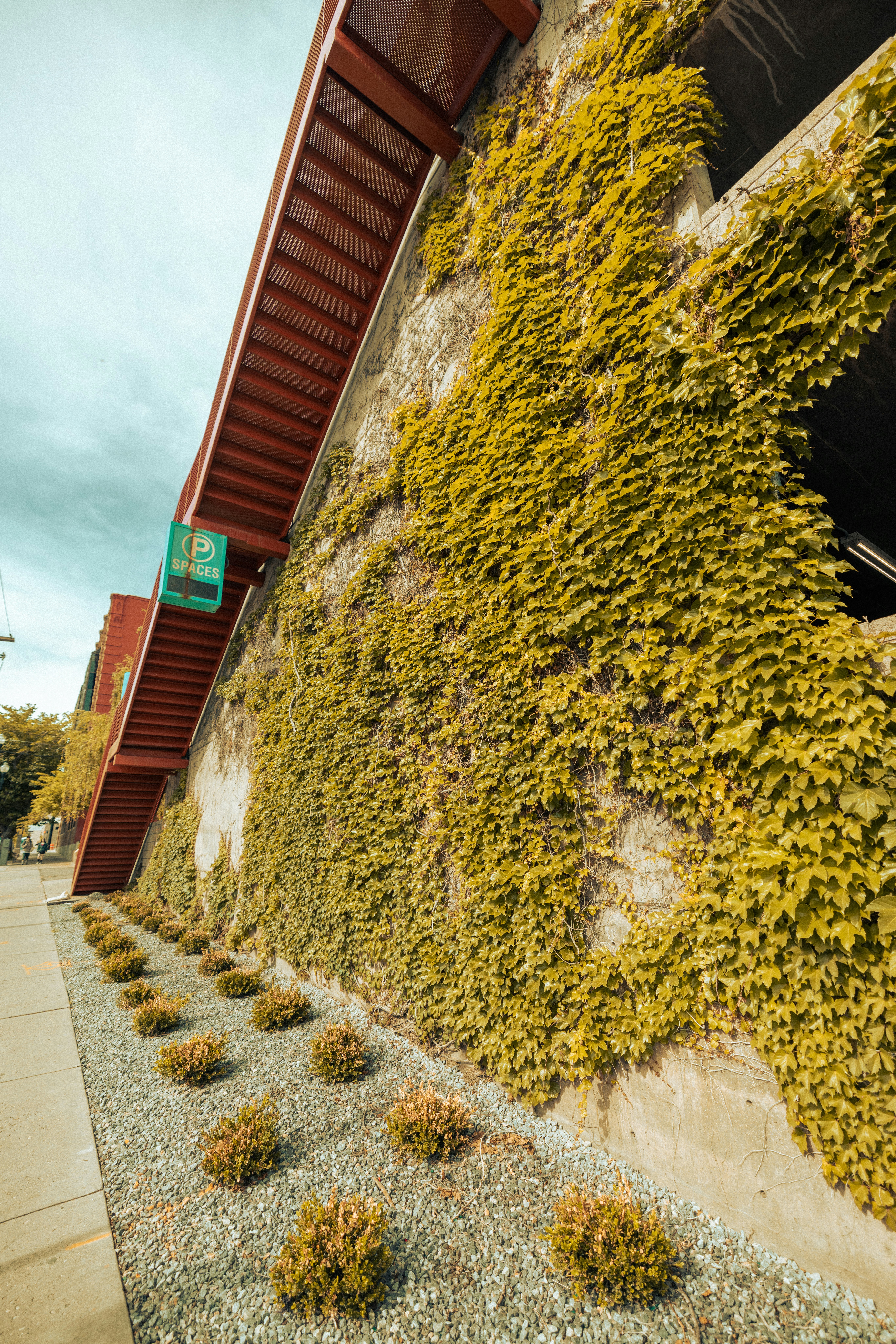 a building covered in green plants next to a sidewalk