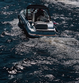 A motorboat travels across dark, choppy waters. The boat leaves a trail of foamy wake behind it, suggesting movement. The vessel appears to be medium-sized, with a canopy overhead.