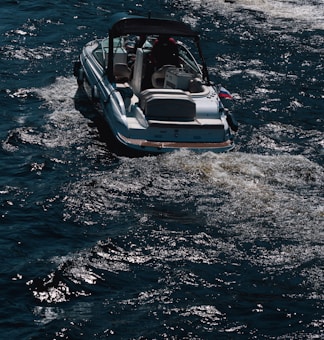 A motorboat travels across dark, choppy waters. The boat leaves a trail of foamy wake behind it, suggesting movement. The vessel appears to be medium-sized, with a canopy overhead.