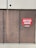 A set of three large brown metal doors with a noticeable sign on the middle door that reads 'Outdoor Centre Customers Enter Here.' The doors show signs of wear and use, with visible scratches and marks. Above the doors is a textured concrete wall.