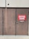 A set of three large brown metal doors with a noticeable sign on the middle door that reads 'Outdoor Centre Customers Enter Here.' The doors show signs of wear and use, with visible scratches and marks. Above the doors is a textured concrete wall.