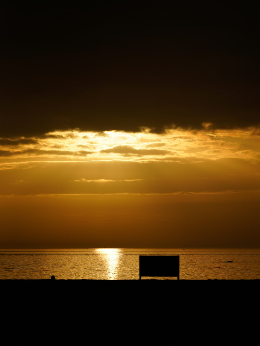 a bench sitting on top of a beach under a cloudy sky