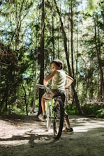 Young rider skillfully balancing on a bright orange bike in a forest clearing.