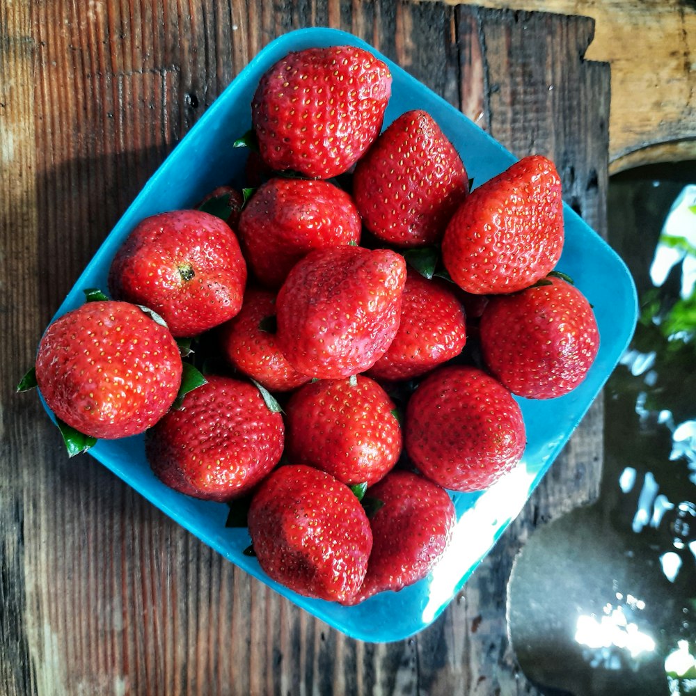 a blue bowl of strawberries on a wooden table