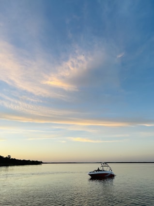 A calm Mazurian lake at sunset with a motorboat gently gliding near Giżycko's marina.